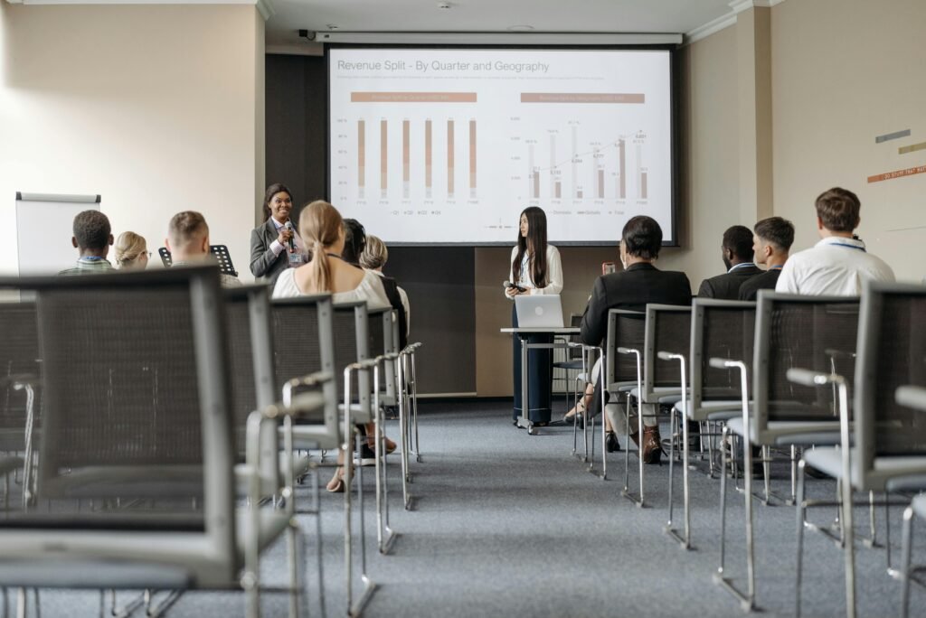 Business conference attendees listen to a presentation on revenue split by quarter and geography.